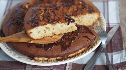 Sliced piece of muffin poured with chocolate icing on a wooden spatula on an ancient wooden background.Homemade healthy food.