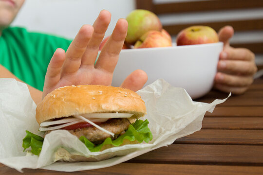 one child's hand pushes the burger away, and the other holds a bowl of apples.Healthcare concept