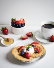 Pancakes with strawberries and blueberries and honey. Light background.