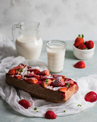 Strawberry cake sprinkled with powdered sugar. Milk in a jug and a glass. Light background.