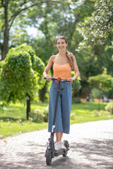 Young girl in orange top riding a scooter in the park and smiling