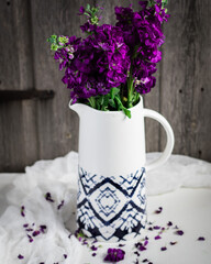 Violet flowers in a white vase on a wooden background.
