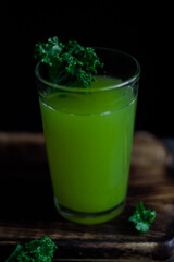 Green drink in a glass with kale on a wooden dark background.