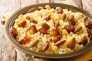 Sweet couscous with almonds, raisins and dates close-up in a plate on the table. Horizontal
