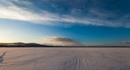 Fototapeta na wymiar frozen lake in winter on a background of blue sky with clouds