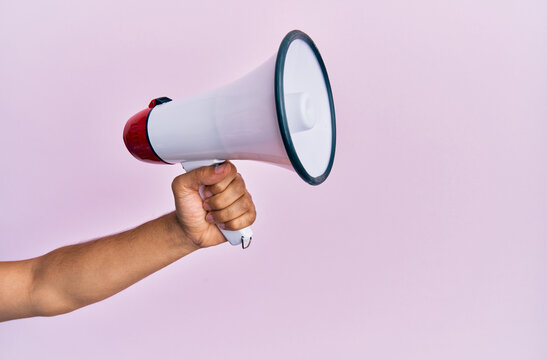 Hand of hispanic man holding megaphone over isolated pink background.