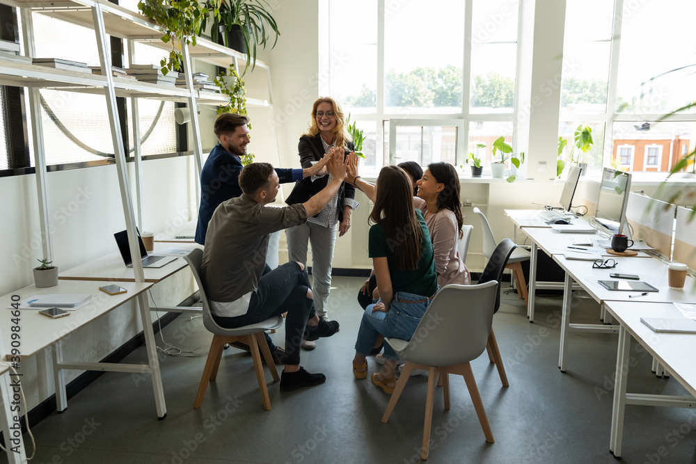 Wall mural Celebrating success. Multiethnic millennial corporate staff and older woman trainer leader stacking hands in high five gesture greeting colleagues with business victory team achievement winning reward