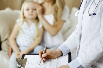 Obraz premium Doctor and patient. Pediatrician using clipboard while examining little girl with her mother at home. Sick and unhappy child at medical exam. Medicine concept