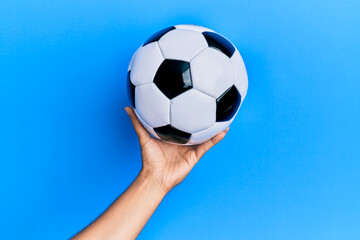 Fototapeta na wymiar Hand of young hispanic man holding soccer ball over isolated blue background.