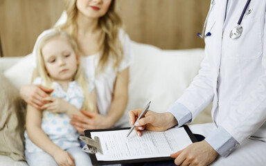 Doctor and patient. Pediatrician using clipboard while examining little girl with her mother at home. Sick and unhappy child at medical exam. Medicine concept