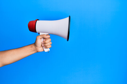 Hand of hispanic man holding megaphone over isolated blue background.