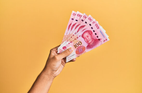 Hand of hispanic man holding chinese 100 yuan banknotes over isolated yellow background.