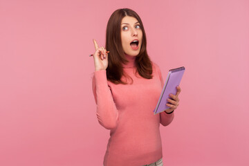 Clever amazed woman with brown hair in pink sweater pointing finger up, having idea to write down...