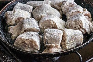 Pieces of fish rolled in flour are fried in a frying pan in oil