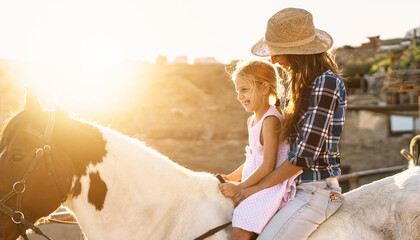 Happy family mother and daughter having fun riding horse inside ranch
