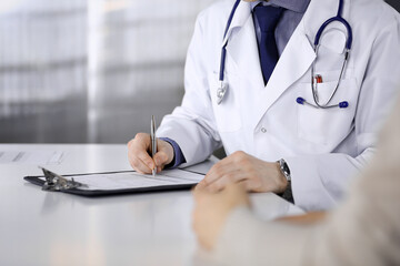 Unknown male doctor and patient woman discussing something while sitting in clinic and using...