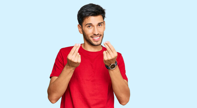 Young handsome man wearing casual red tshirt doing money gesture with hands, asking for salary payment, millionaire business