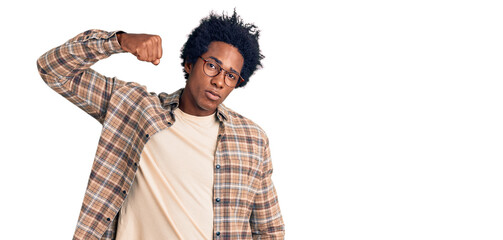 Handsome african american man with afro hair wearing casual clothes and glasses strong person showing arm muscle, confident and proud of power