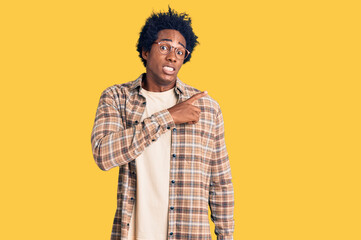 Handsome african american man with afro hair wearing casual clothes and glasses pointing aside worried and nervous with forefinger, concerned and surprised expression