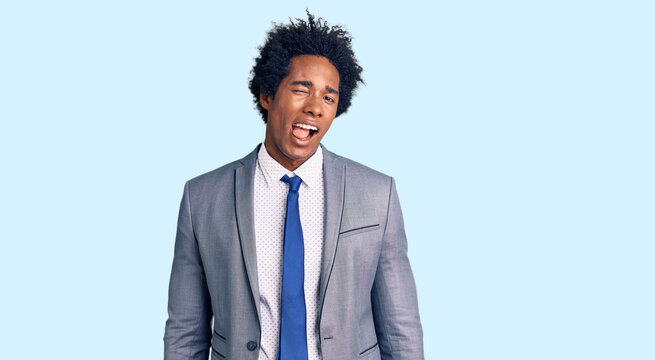 Handsome african american man with afro hair wearing business jacket winking looking at the camera with sexy expression, cheerful and happy face.