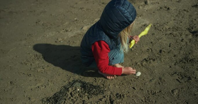 A preschooler is playing on the beach with a spade in the autumn