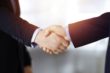 Business people shaking hands, close-up. Group of unknown businessmen standing in a sunny modern office. Teamwork, partnership and handshake concept