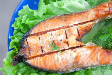 Roasted trout steak on lettuce leaves on a blue plate close-up