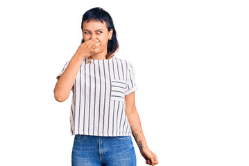 Young woman wearing casual clothes smelling something stinky and disgusting, intolerable smell,...