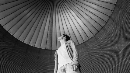 Grayscale shot of a young male wearing a white t-shirt paired with jeans and a jacket in a building