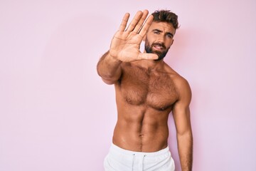 Young hispanic man standing shirtless doing stop sing with palm of the hand. warning expression...