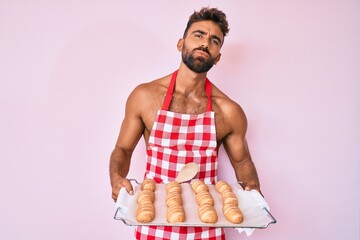 Young hispanic man shirtless wearing baker uniform holding homemade bread looking at the camera blowing a kiss being lovely and sexy. love expression. - obrazy, fototapety, plakaty