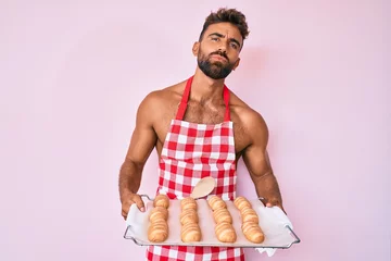 Foto op Plexiglas Young hispanic man shirtless wearing baker uniform holding homemade bread looking at the camera blowing a kiss being lovely and sexy. love expression. © Krakenimages.com