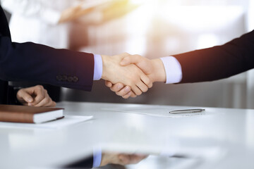 Business people shaking hands at meeting or negotiation, close-up. Group of unknown businessmen sitting at the desk in a sunny modern office. Teamwork and partnership concept
