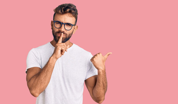 Young hispanic man wearing casual clothes and glasses asking to be quiet with finger on lips pointing with hand to the side. silence and secret concept.