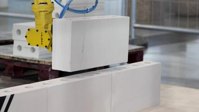 Industrial robotic machine at the industrial international exhibition. Media. Close up of a robot putting a white brick in a layer of a wall, technologies for urban construction site.