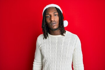 African american man with braids wearing christmas hat relaxed with serious expression on face. simple and natural looking at the camera.