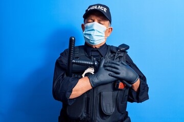 Senior police man wearing surgical mask smiling with hands on chest with closed eyes and grateful...