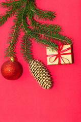 Natural spruce tree branch with a fir cone and Christmas decorations on a red background. Merry christmas and New Year. A minimalist composition, celebration and giving gifts. Copy space, flat lay.