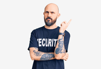 Young handsome man wearing security t shirt pointing with hand finger to the side showing advertisement, serious and calm face