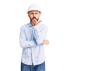 Young handsome man wearing architect hardhat looking at the camera blowing a kiss with hand on air being lovely and sexy. love expression.
