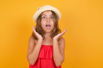 Indoor closeup of young Caucasian girl standing against yellow background holding hands under chin feeling excited about new plans. 