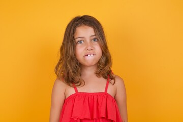 young Caucasian girl standing against yellow background being nervous and scared biting lips...