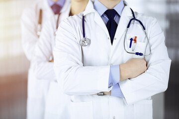 Group of modern doctors standing as a team with crossed arms and stethoscopes in a sunny hospital office. Physicians ready to examine and help patients. Medical help, insurance in health care, best