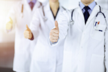 Group of unknown doctors stand as a team with thumbs up in a sunny hospital office. Physicians ready to examine and help patients. Medical help, insurance in health care, best desease treatment and