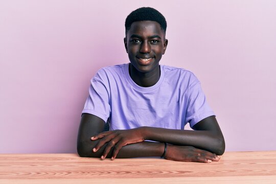 Young african american man wearing casual clothes sitting on the table looking positive and happy standing and smiling with a confident smile showing teeth
