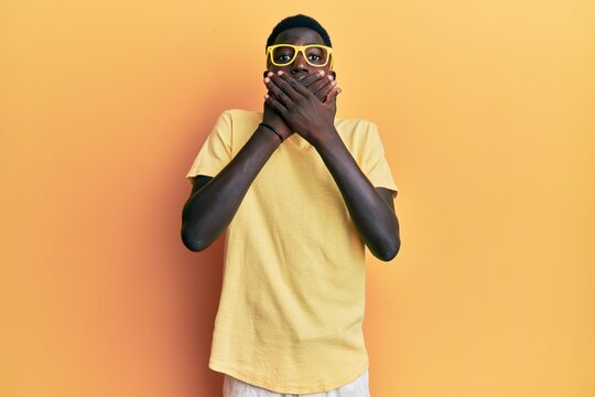 Young african american man wearing casual clothes and glasses shocked covering mouth with hands for mistake. secret concept.