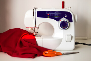 The sewing machine is on a white table. The red fabric is ready to go.