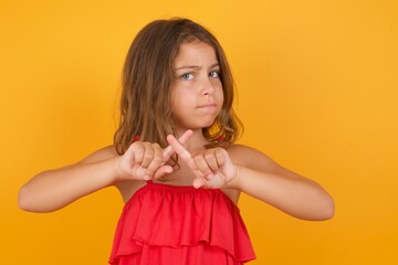 Caucasian young girl standing against yellow background has rejection angry expression crossing...