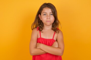 Portrait of young Caucasian girl standing against yellow background with positive expression, has crossed arms, feels happy and confident.