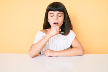 Young little girl with bang wearing casual clothes sitting on the table feeling unwell and coughing as symptom for cold or bronchitis. health care concept.